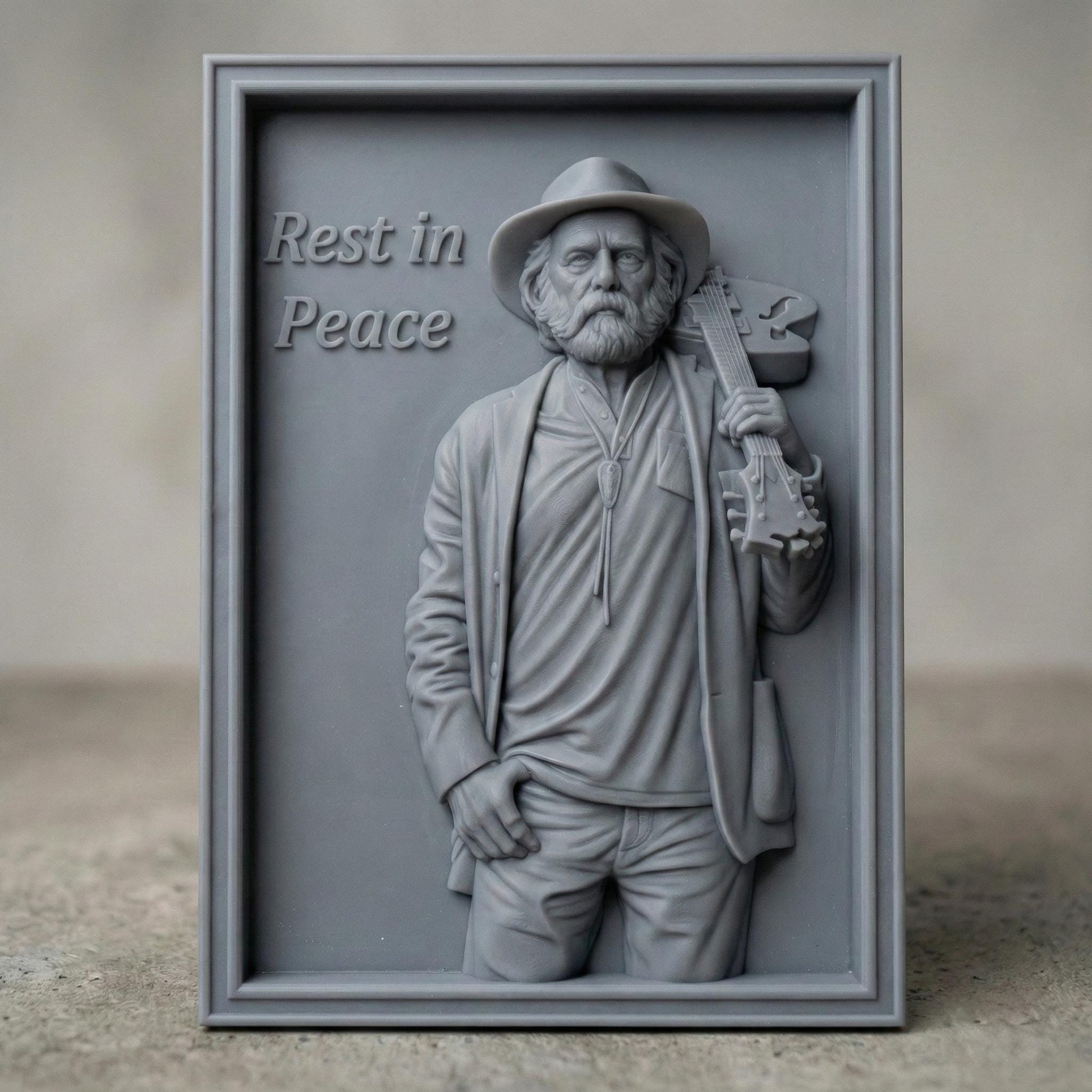 Detailed 3D relief sculpture of an elderly bearded musician wearing a hat and jacket, holding an acoustic guitar over his shoulder. The figure is carved in a realistic wood-grain style with expressive facial features and deep folds in clothing. A framed bas-relief version includes the engraved text “Rest in Peace,” creating a solemn memorial tribute suited for CNC carving, 3D printing, and wall art display.