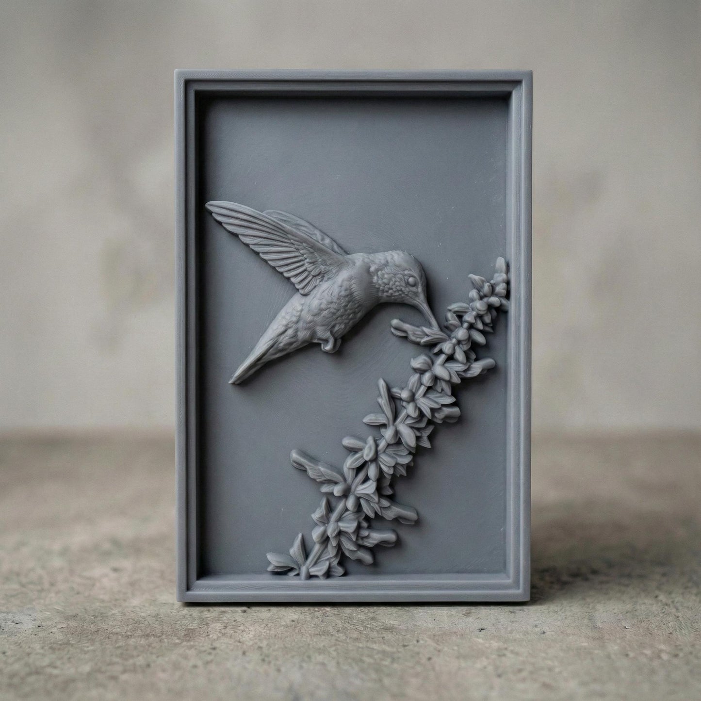 Elegant hummingbird bas relief STL depicting a hummingbird in flight feeding from cascading bell-shaped flowers, carved within a refined rectangular frame. The design features flowing leaves, delicate floral textures, and detailed feathers set against a smooth wood-grain background. Ideal for CNC wood carving, 3D printing, or framed wall art panels inspired by botanical and wildlife themes.