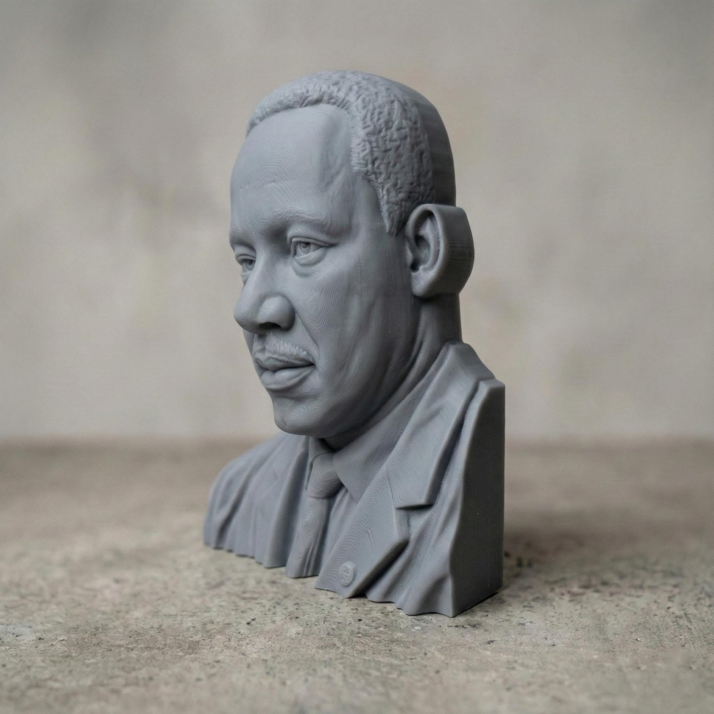 Highly detailed 3D portrait bust of Martin Luther King Jr., depicted with a calm, thoughtful expression and formal suit and tie. Rendered in a realistic wood-carved style, the sculpture emphasizes facial depth, historical dignity, and symbolic leadership. Ideal for Martin Luther King Jr. Day displays, educational settings, memorial art, CNC carving, and 3D printing projects honoring civil rights history.