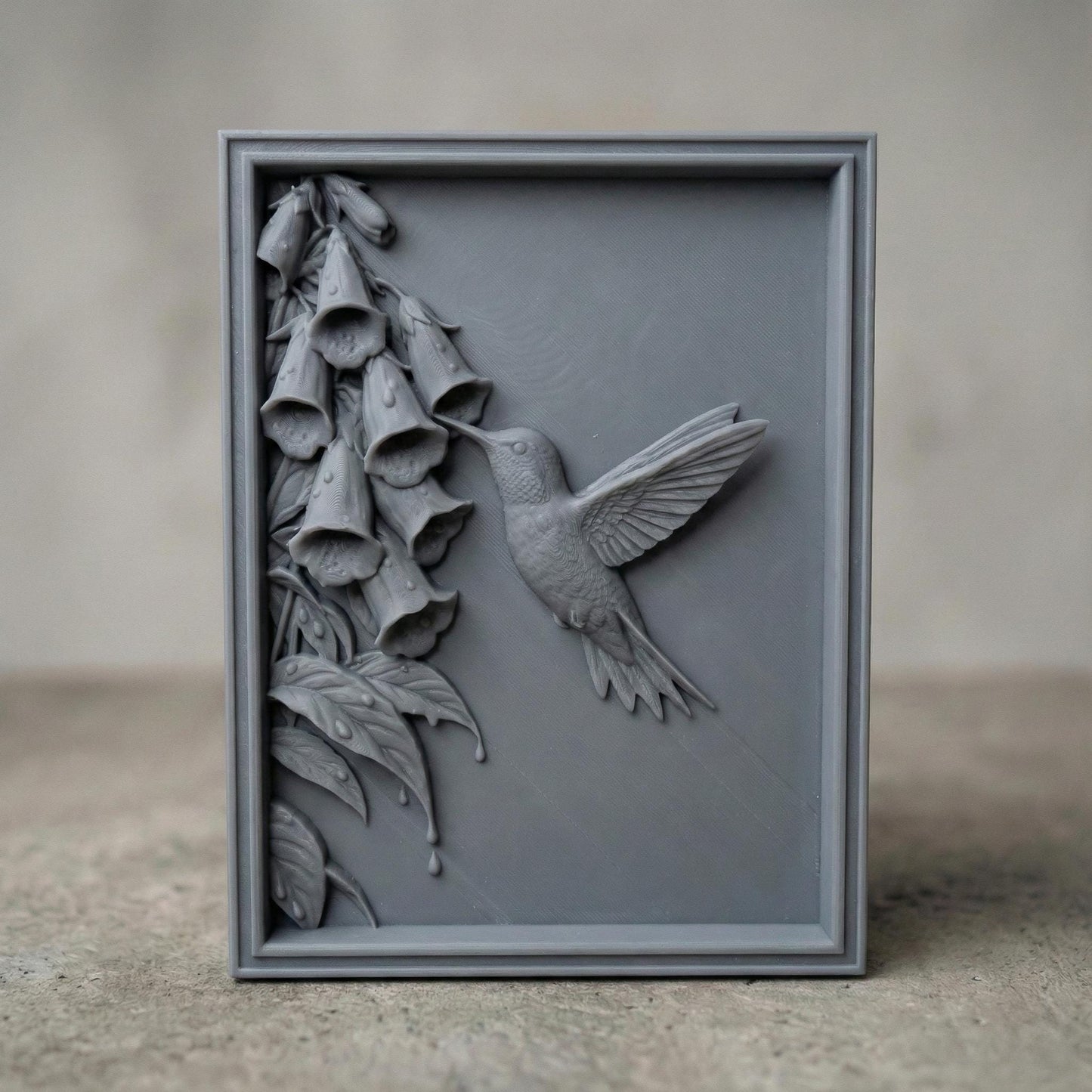 Elegant hummingbird bas relief STL depicting a hummingbird in flight feeding from cascading bell-shaped flowers, carved within a refined rectangular frame. The design features flowing leaves, delicate floral textures, and detailed feathers set against a smooth wood-grain background. Ideal for CNC wood carving, 3D printing, or framed wall art panels inspired by botanical and wildlife themes.