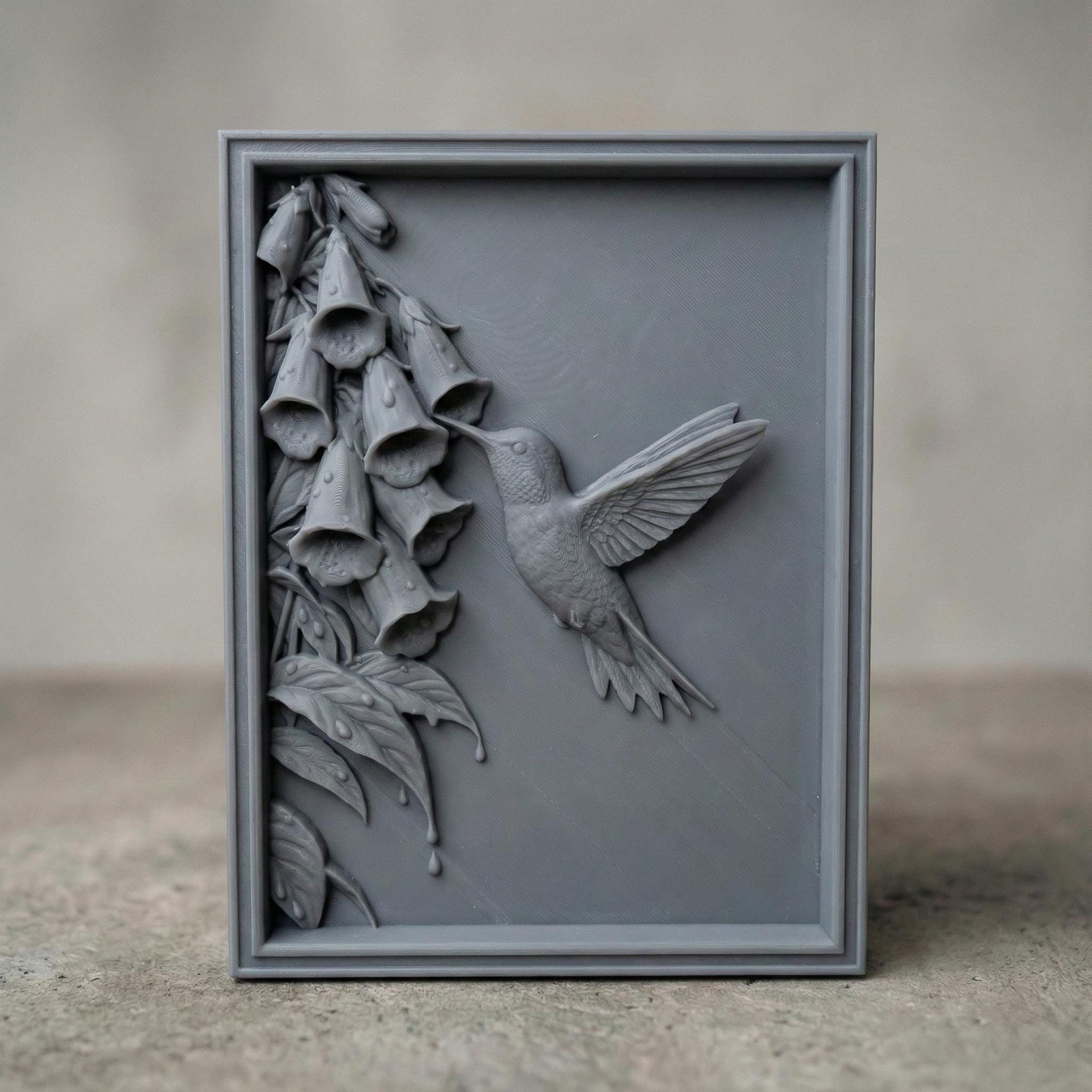 Elegant hummingbird bas relief STL depicting a hummingbird in flight feeding from cascading bell-shaped flowers, carved within a refined rectangular frame. The design features flowing leaves, delicate floral textures, and detailed feathers set against a smooth wood-grain background. Ideal for CNC wood carving, 3D printing, or framed wall art panels inspired by botanical and wildlife themes.