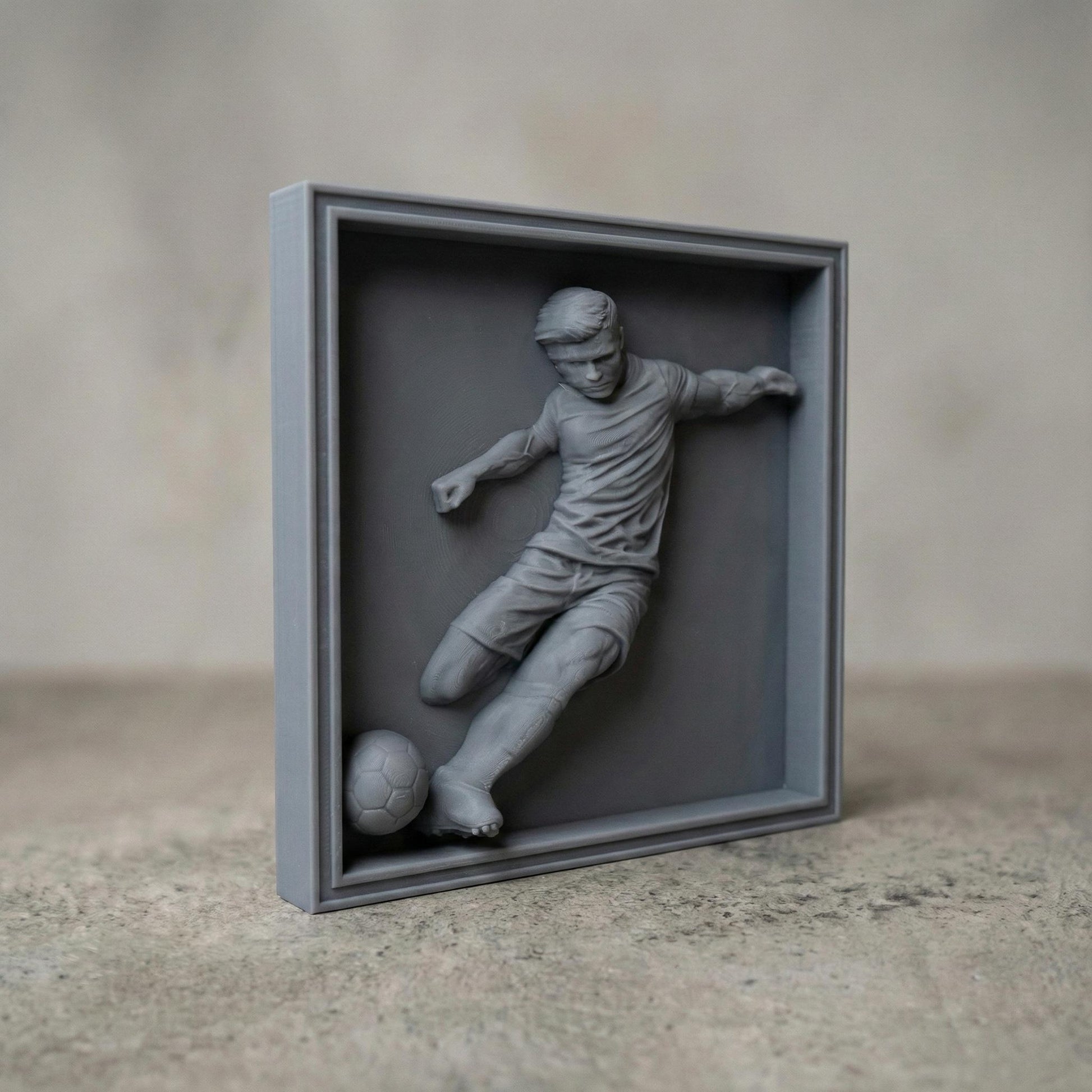 Detailed bas-relief sculpture of a soccer player captured mid-kick, shown as a realistic carved wooden relief with dynamic motion, muscular anatomy, flowing clothing folds, and a soccer ball at the foot. The design features deep relief depth, clean contours, and smooth transitions ideal for CNC carving, 3D printing, or router engraving as decorative sports wall art.