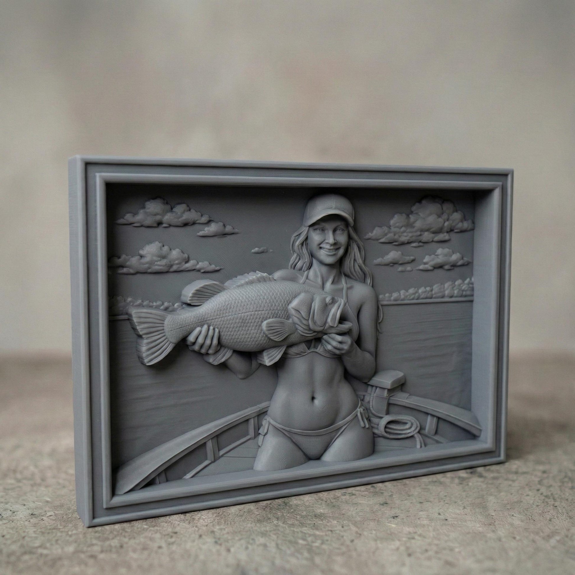 Detailed bas-relief carving of a smiling female angler holding a large bass fish while standing on a boat. The scene features calm lake water, carved clouds in the sky, and realistic wood grain texture. The rectangular framed panel highlights fine details in the fish scales, facial expression, and boat elements, designed for CNC carving or 3D printing as rustic fishing wall decor.