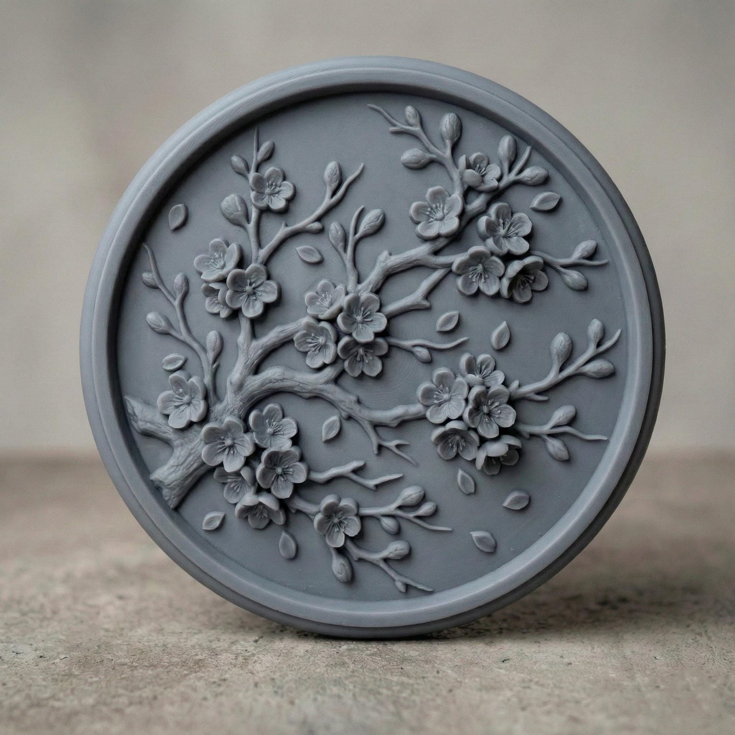Circular bas-relief panel featuring an elegant cherry blossom branch in full bloom, with layered petals, delicate buds, and gently scattered leaves. The flowing branch curves organically across a textured woodgrain background, framed by a smooth round border. Deep carving creates soft shadows and dimensional detail, ideal for CNC carving, 3D printing, spring décor, and botanical wall art projects.
