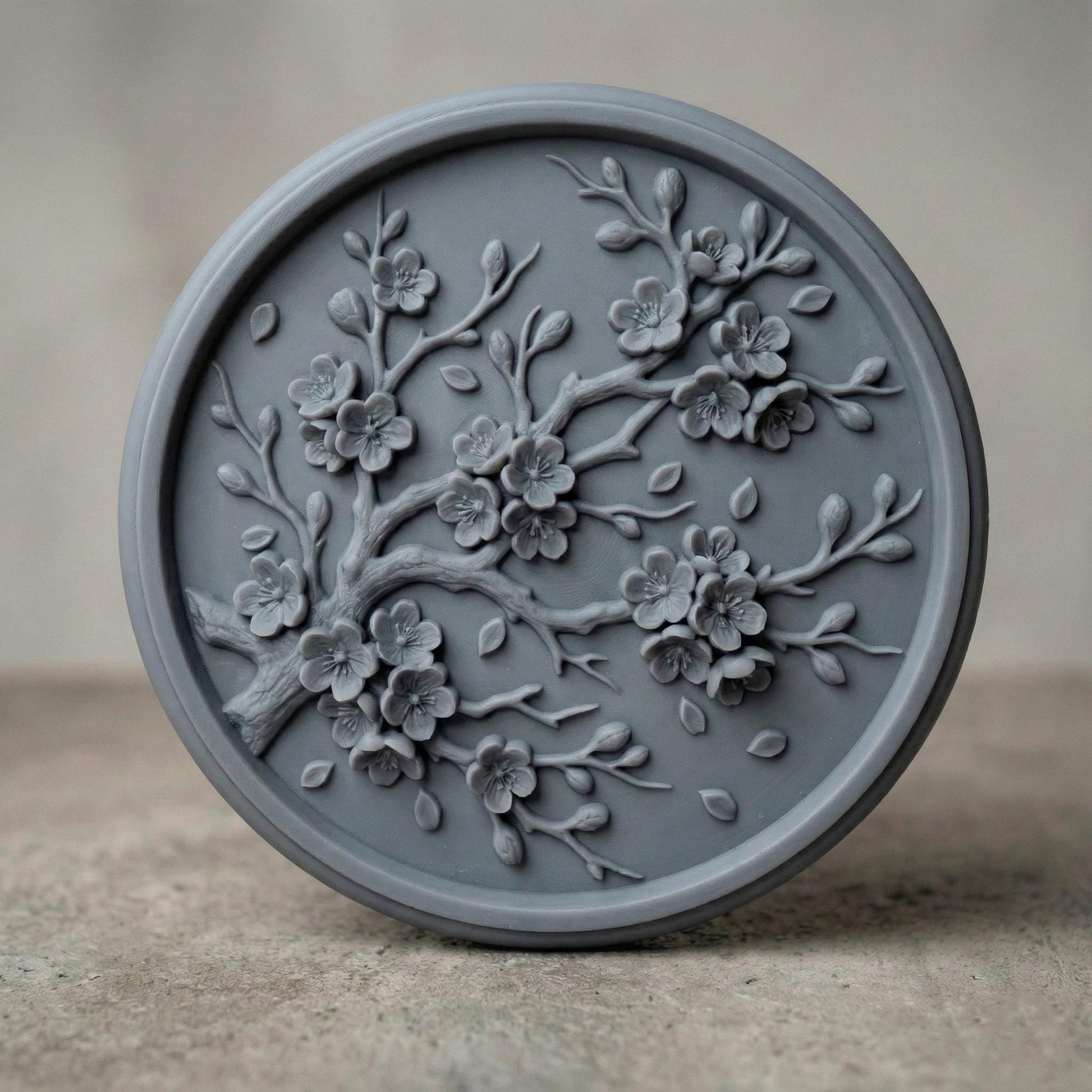Circular bas-relief panel featuring an elegant cherry blossom branch in full bloom, with layered petals, delicate buds, and gently scattered leaves. The flowing branch curves organically across a textured woodgrain background, framed by a smooth round border. Deep carving creates soft shadows and dimensional detail, ideal for CNC carving, 3D printing, spring décor, and botanical wall art projects.