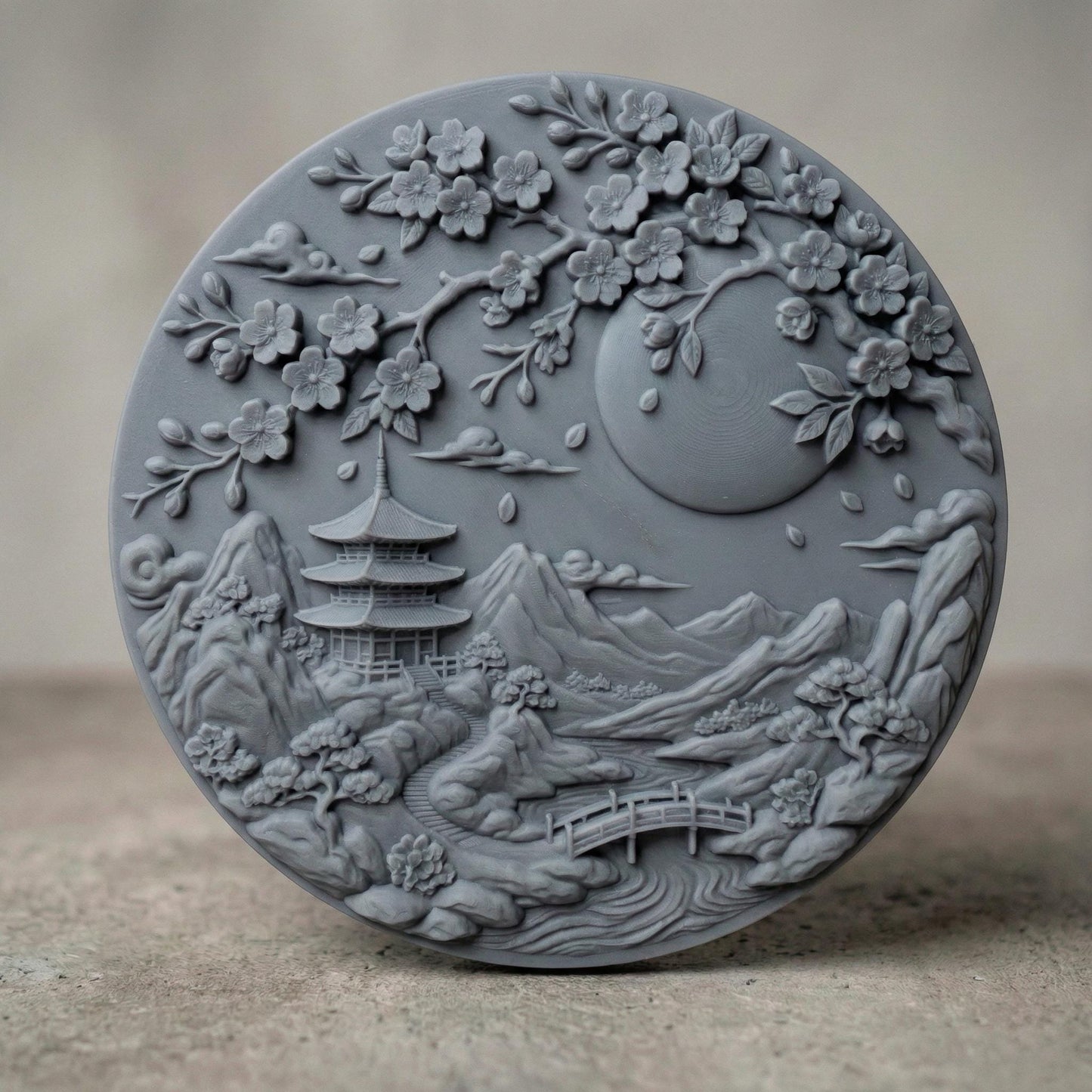 Intricate round bas-relief featuring a serene Japanese landscape with tiered pagoda temple, flowing river, arched wooden bridge, layered mountain peaks, and drifting clouds beneath a large full moon. Cherry blossom branches frame the top with detailed petals and falling leaves. Deep carving and textured contours create dimensional shadows, ideal for CNC carving, 3D printing, and tranquil Zen-inspired wall décor.