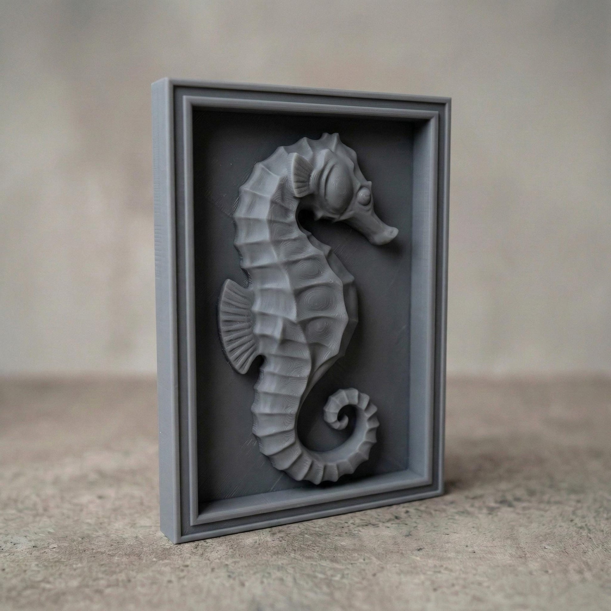 Detailed bas-relief seahorse carving mounted inside a rectangular wooden frame, featuring layered scales, curved tail, and textured dorsal ridges. The marine creature is sculpted in a relief style suitable for CNC carving or 3D printing, creating elegant coastal wall decor inspired by ocean life and nautical themes.