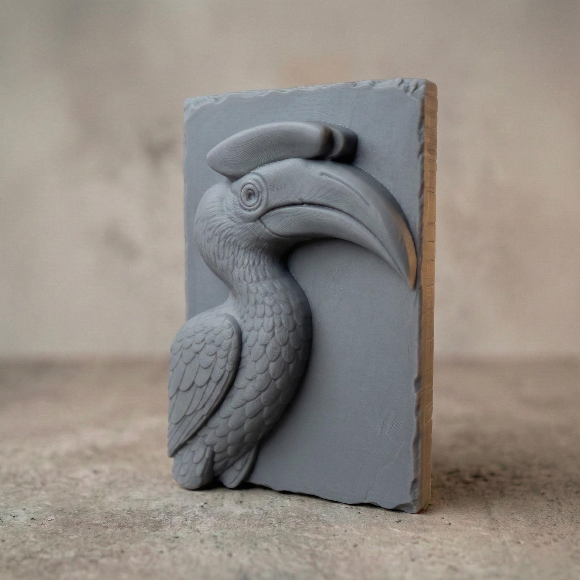 Detailed bas-relief carving of a hornbill bird head with a large curved beak and distinctive casque, sculpted with layered feathers and smooth contours. The tropical wildlife design is carved on a natural wood slab style background with organic edges, creating elegant jungle-inspired spring and summer wall art suitable for CNC carving or 3D printing.