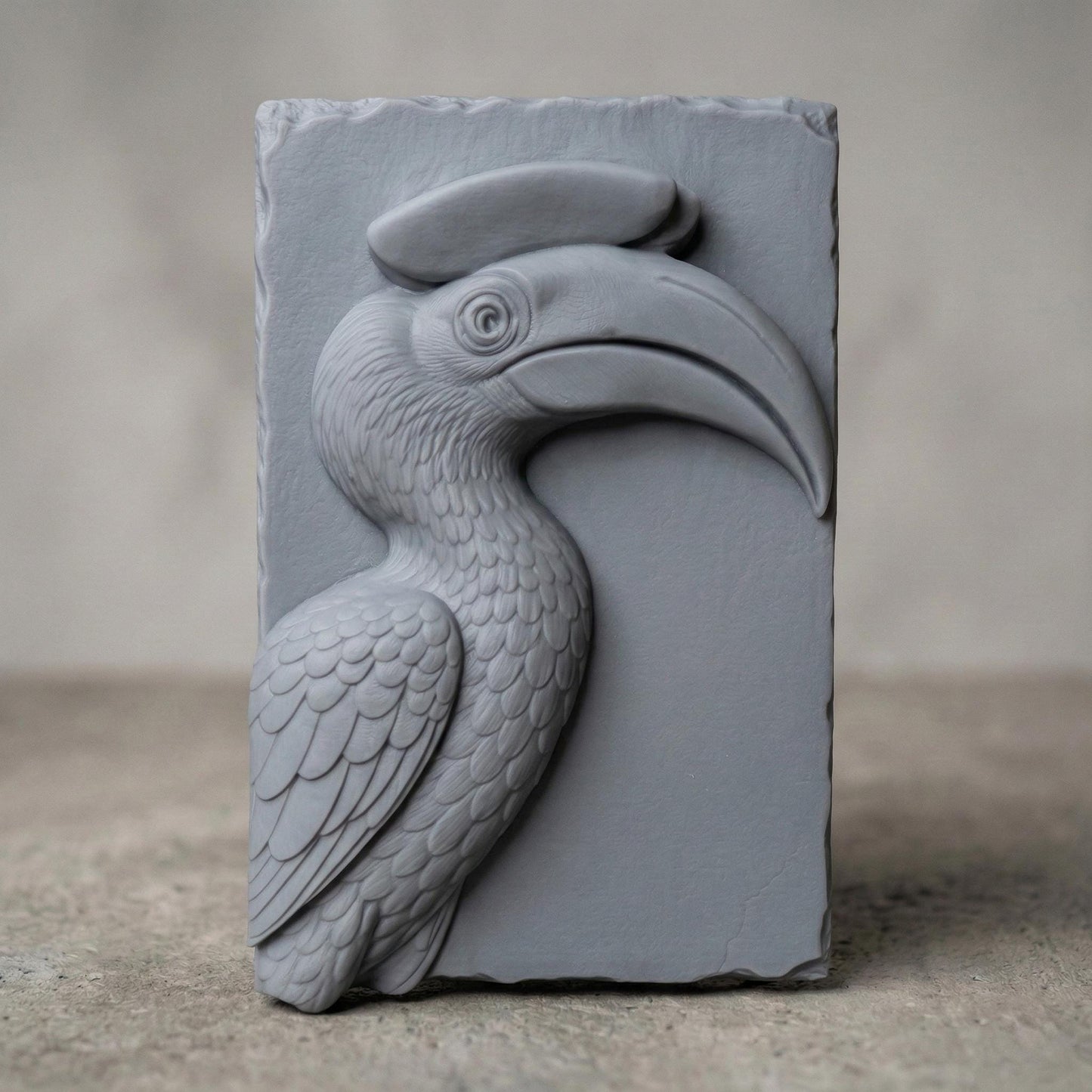 Detailed bas-relief carving of a hornbill bird head with a large curved beak and distinctive casque, sculpted with layered feathers and smooth contours. The tropical wildlife design is carved on a natural wood slab style background with organic edges, creating elegant jungle-inspired spring and summer wall art suitable for CNC carving or 3D printing.