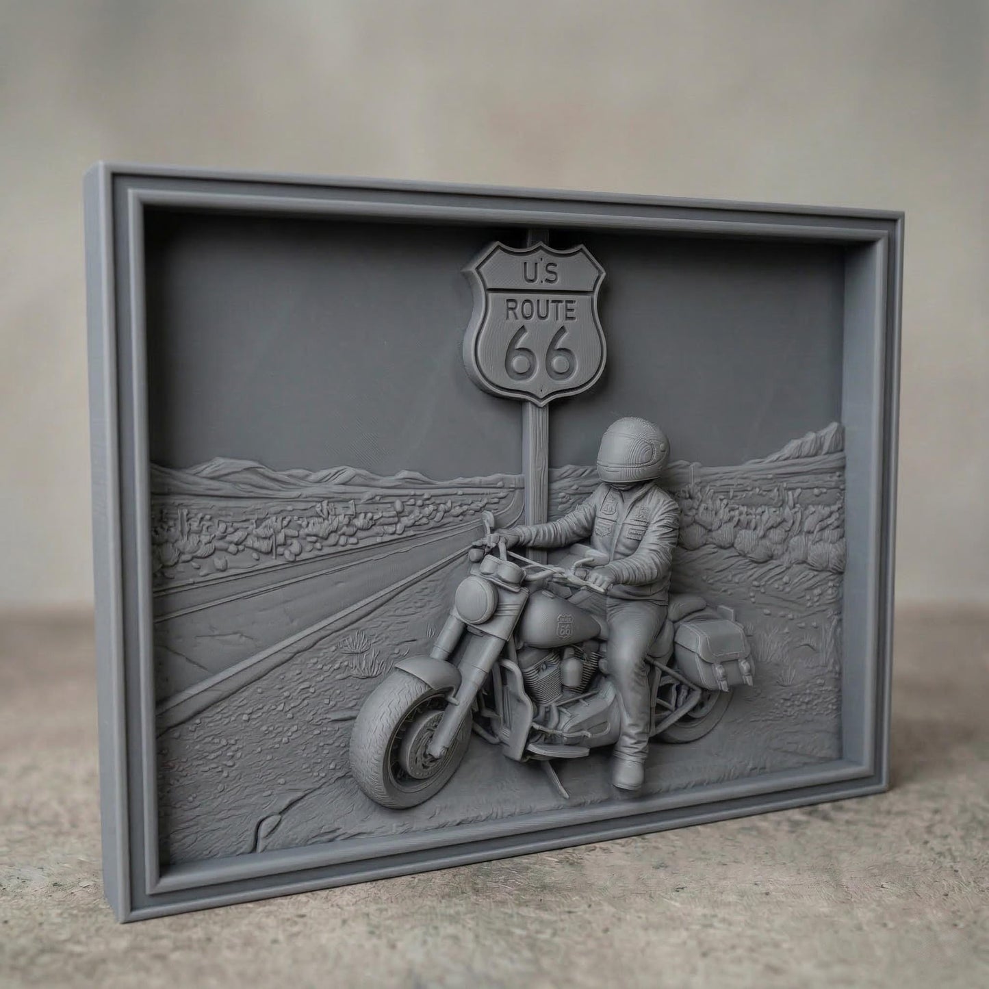 Detailed bas-relief scene of a motorcycle rider parked beside a US Route 66 road sign in a desert highway landscape. The rider wears a helmet and leather riding gear while sitting on a classic touring motorcycle with saddlebags. The background shows an open road stretching through desert terrain with cacti and distant mountains, symbolizing freedom, adventure, and the iconic American road trip culture.