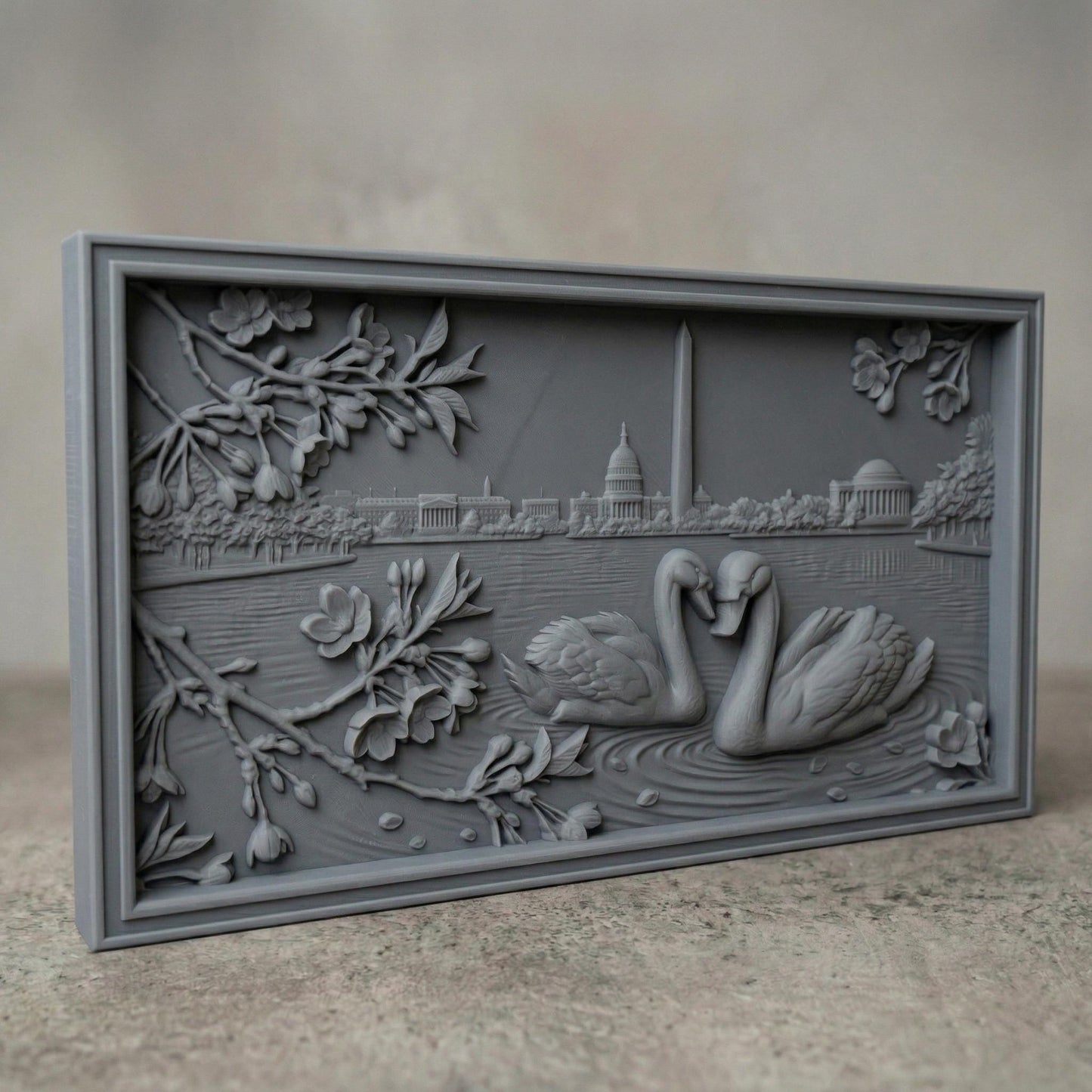 Detailed bas-relief carving of two swans forming a heart shape on rippling water, surrounded by blossoming branches. In the background, the Washington Monument and Capitol building rise along a serene lakeside skyline. Fine wood grain texture and layered depth create an elegant, romantic composition symbolizing love and unity in a peaceful natural setting.