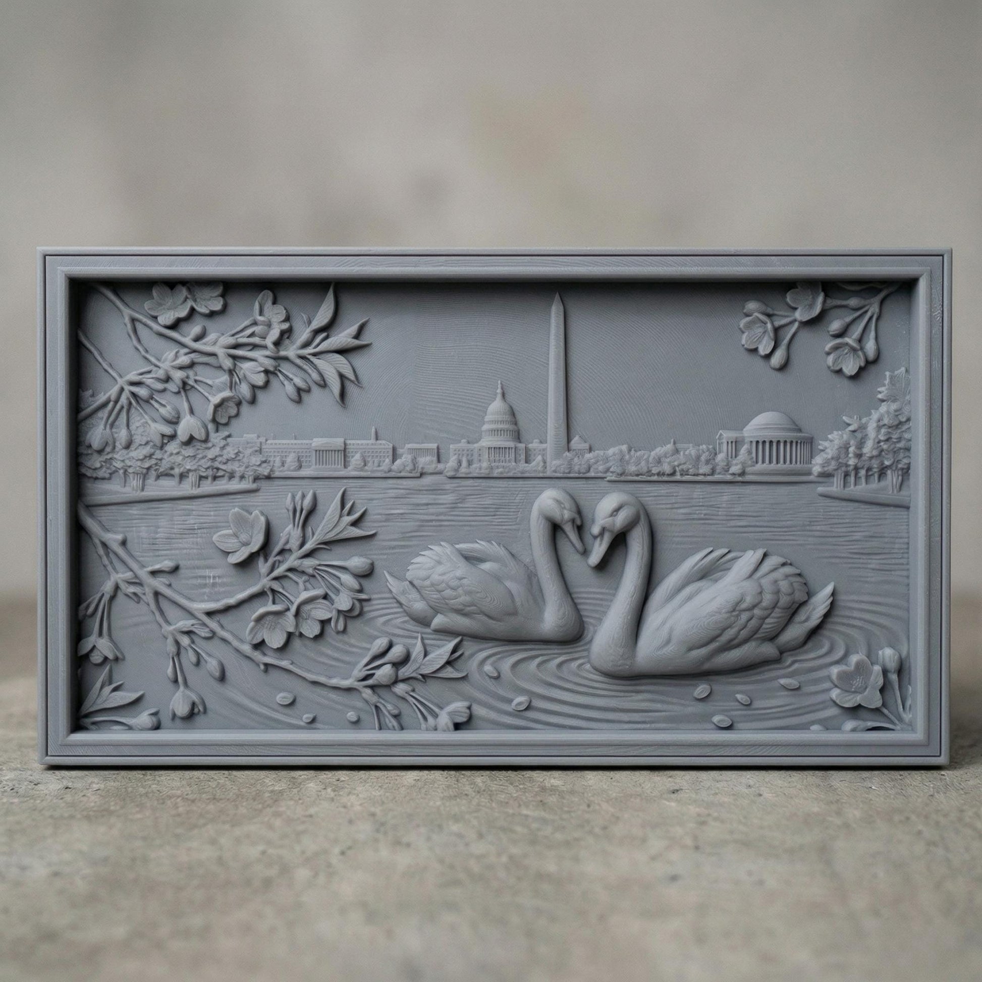 Detailed bas-relief carving of two swans forming a heart shape on rippling water, surrounded by blossoming branches. In the background, the Washington Monument and Capitol building rise along a serene lakeside skyline. Fine wood grain texture and layered depth create an elegant, romantic composition symbolizing love and unity in a peaceful natural setting.