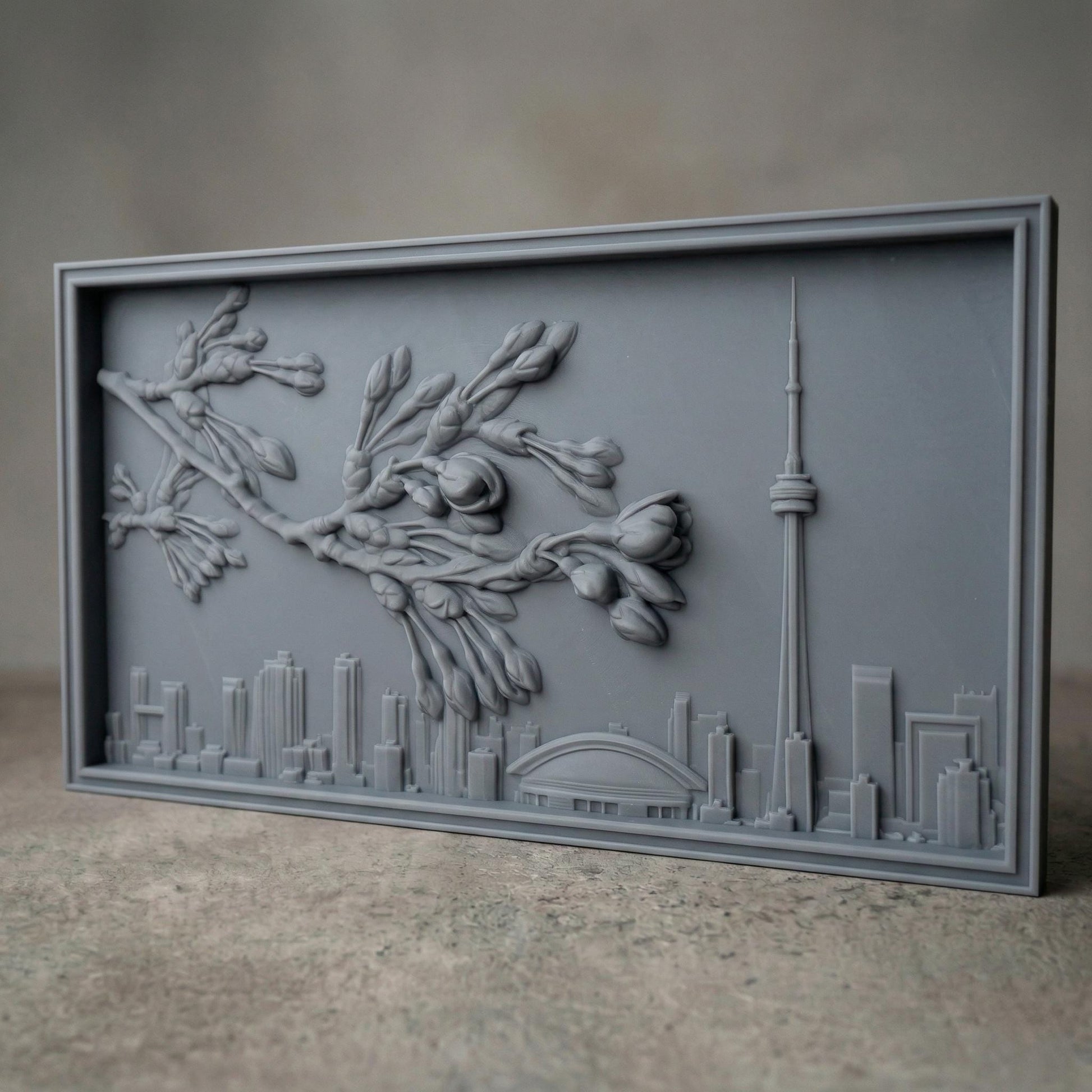 Elegant bas-relief carving of Toronto skyline featuring the CN Tower and Rogers Centre beneath a detailed cherry blossom branch in full spring bloom. The blossoms stretch across the scene above layered city buildings, with rich wood grain texture and smooth depth creating a harmonious blend of urban architecture and natural beauty.