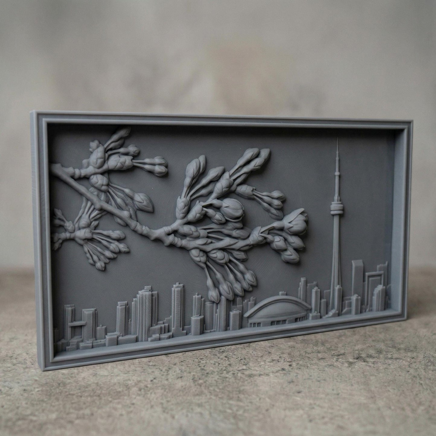 Elegant bas-relief carving of Toronto skyline featuring the CN Tower and Rogers Centre beneath a detailed cherry blossom branch in full spring bloom. The blossoms stretch across the scene above layered city buildings, with rich wood grain texture and smooth depth creating a harmonious blend of urban architecture and natural beauty.