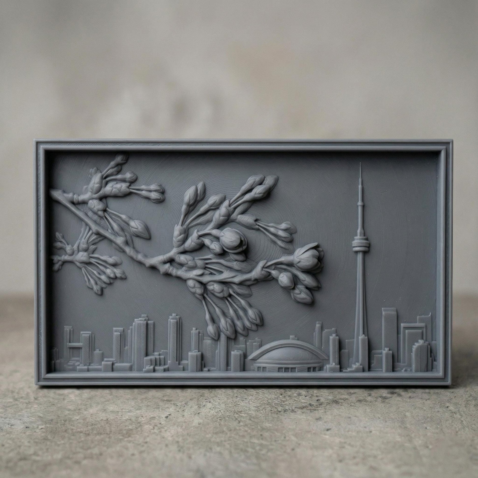 Elegant bas-relief carving of Toronto skyline featuring the CN Tower and Rogers Centre beneath a detailed cherry blossom branch in full spring bloom. The blossoms stretch across the scene above layered city buildings, with rich wood grain texture and smooth depth creating a harmonious blend of urban architecture and natural beauty.