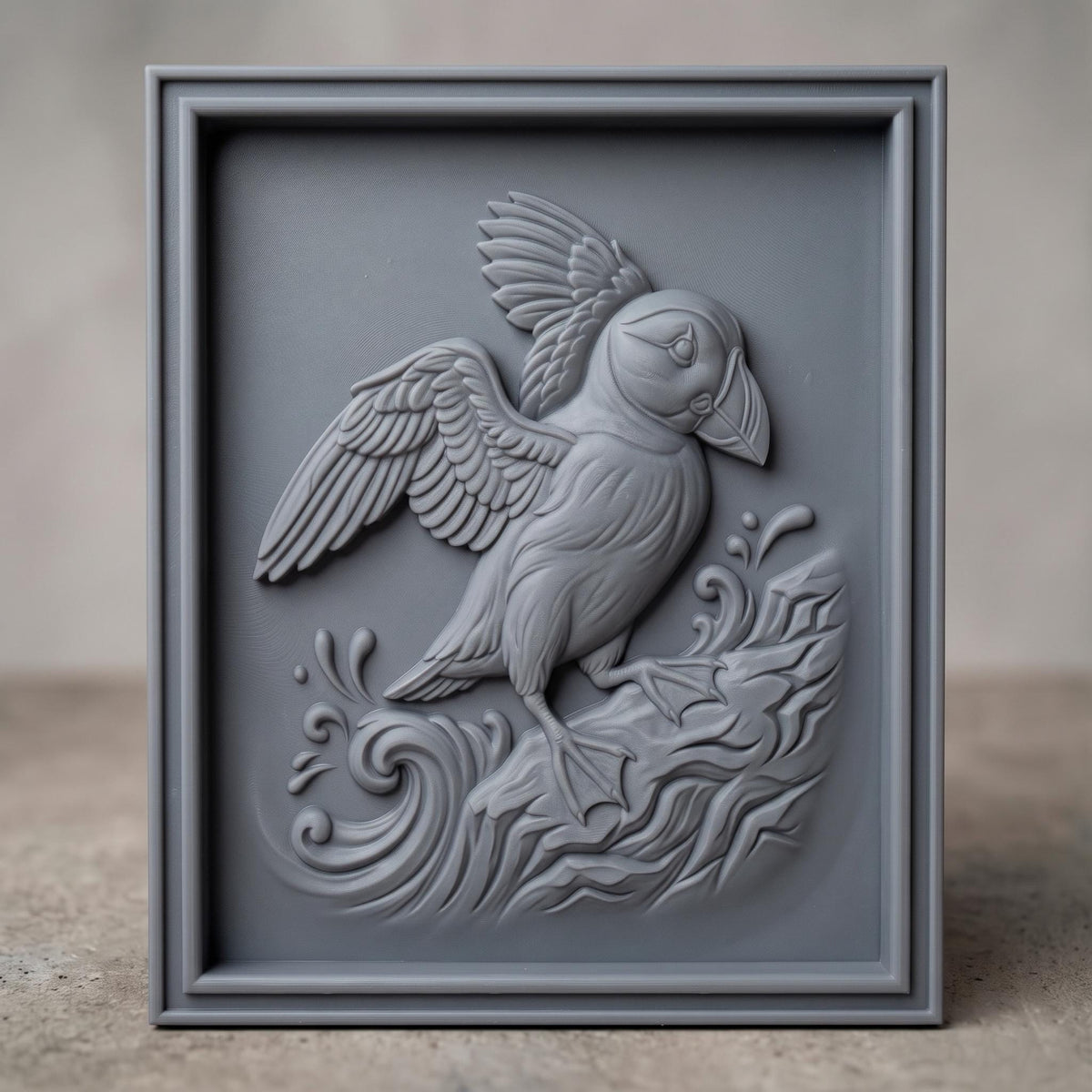 Detailed 3D bas-relief of an Atlantic puffin with wings spread, standing on a rocky cliff amid splashing ocean waves and swirling water patterns. Carved in rich walnut wood grain with fine feather texture and a raised beak, set within a rectangular frame border. Designed for CNC relief carving, wood routing, resin casting, and 3D printing as coastal wall decor.