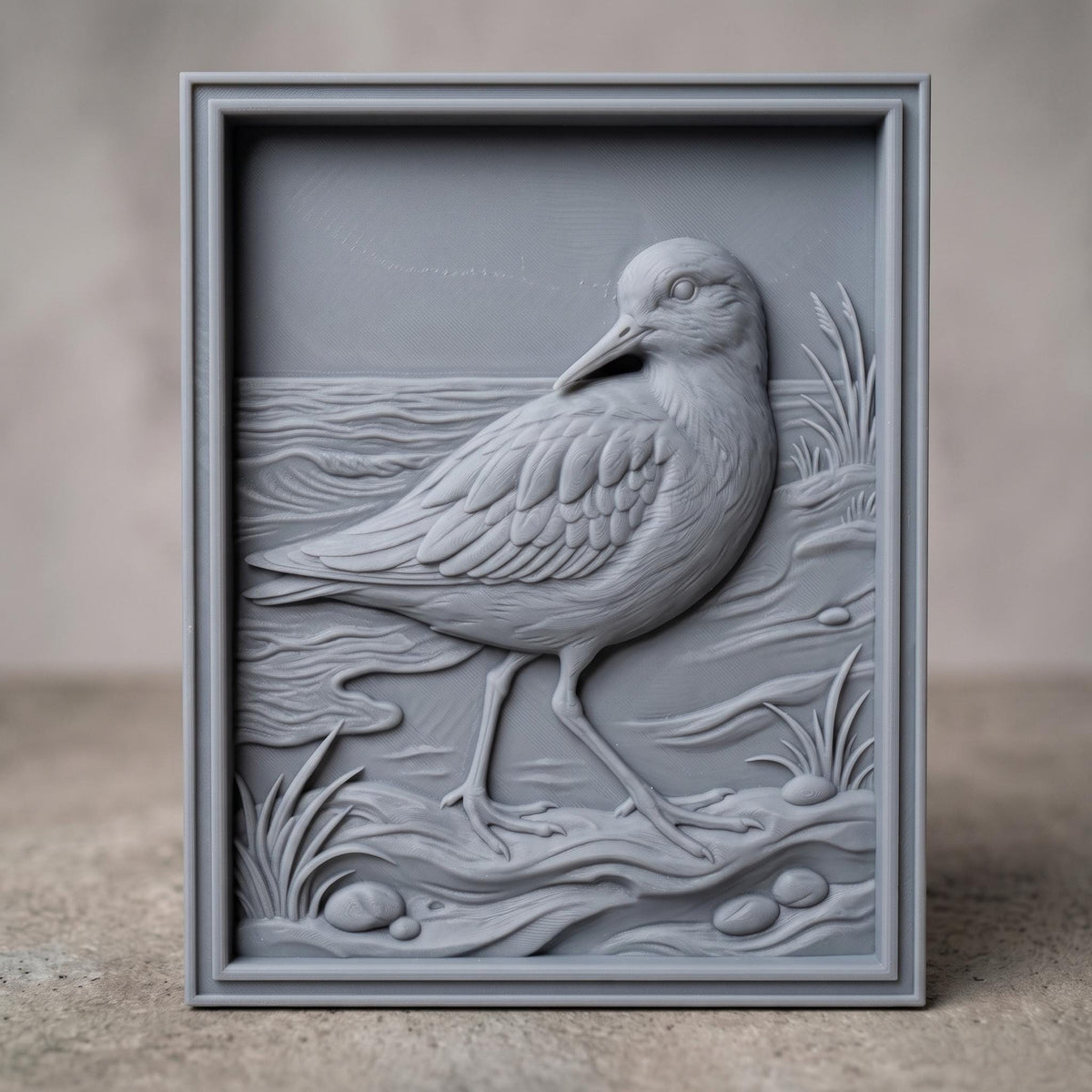 Detailed 3D bas-relief of a sandpiper walking along a shoreline, long slender bill and layered wing feathers, mid-stride on wet sand. Rippling water, scattered pebbles and tufts of marsh grass fill the scene, all set within a raised rectangular frame border. Designed for CNC relief carving, wood routing, resin casting, and 3D printing as coastal wall decor.