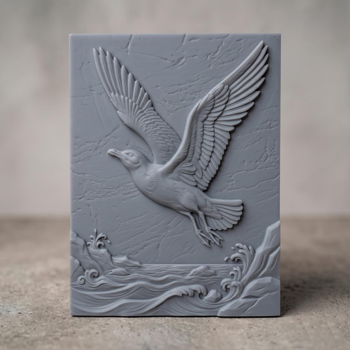 3D bas-relief of a seagull in flight, wings fully spread, soaring above cresting ocean waves and a rocky shoreline. Fine feather detailing and natural stone-like texture cover the rectangular panel background, with carved wave crests and splashing surf along the base. Designed for CNC relief carving, wood routing, resin casting, and 3D printing as coastal wall decor.