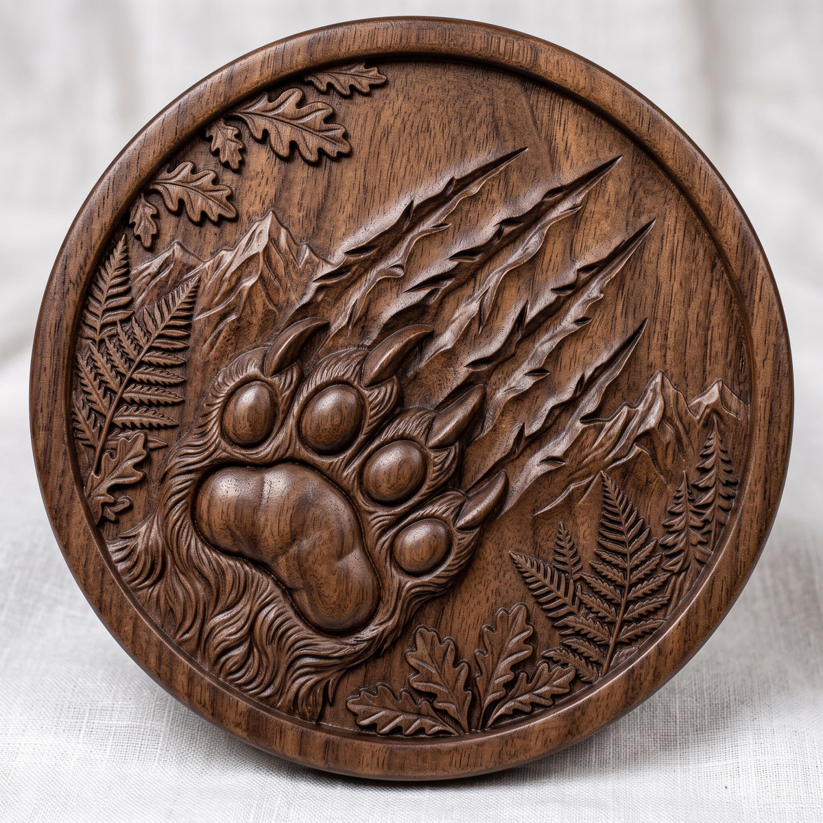 Detailed 3D bas-relief of a large bear paw with four toe pads and curved claws, with deep claw scratch marks slashing across a round medallion. Mountain peaks, ferns, oak leaves and pine trees fill the scene inside a raised ring border. Shown in carved walnut wood and grey resin. Designed for CNC relief carving, woodworking and 3D printing as rustic cabin wildlife wall decor.
