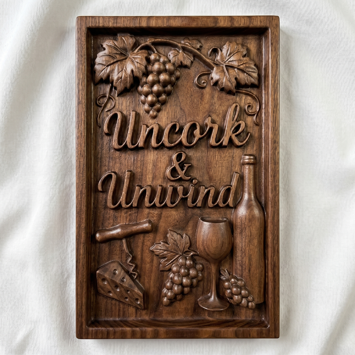 Detailed wooden bas-relief featuring the phrase “Uncork & Unwind” surrounded by grape clusters, vine leaves, a wine bottle, glass, corkscrew, and cheese wedge. The composition includes flowing script text, layered textures, and a framed rustic design, perfect for wine lovers and ideal for CNC carving or 3D printing decorative kitchen or bar wall art.