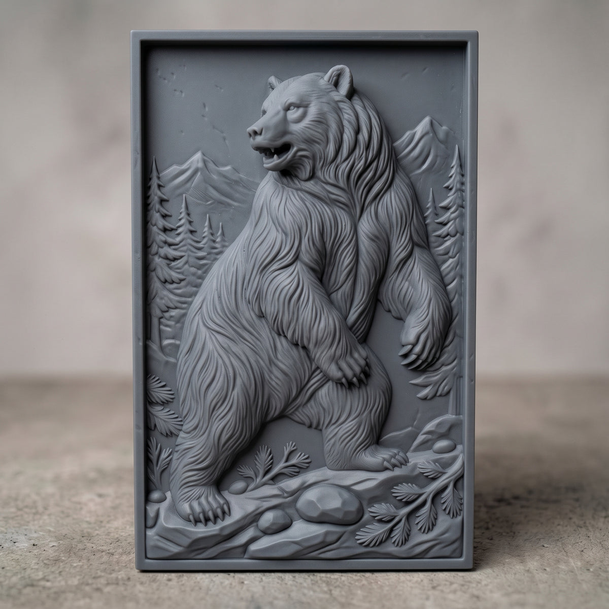 Detailed 3D bas-relief of a standing grizzly bear in a pine forest with snow-capped mountains behind, rocky ground and fern details in the foreground. Framed by a rectangular molded border around a recessed panel. Shown in carved walnut wood and grey resin. Designed for CNC relief carving, woodworking and 3D printing as rustic cabin and wildlife wall decor.