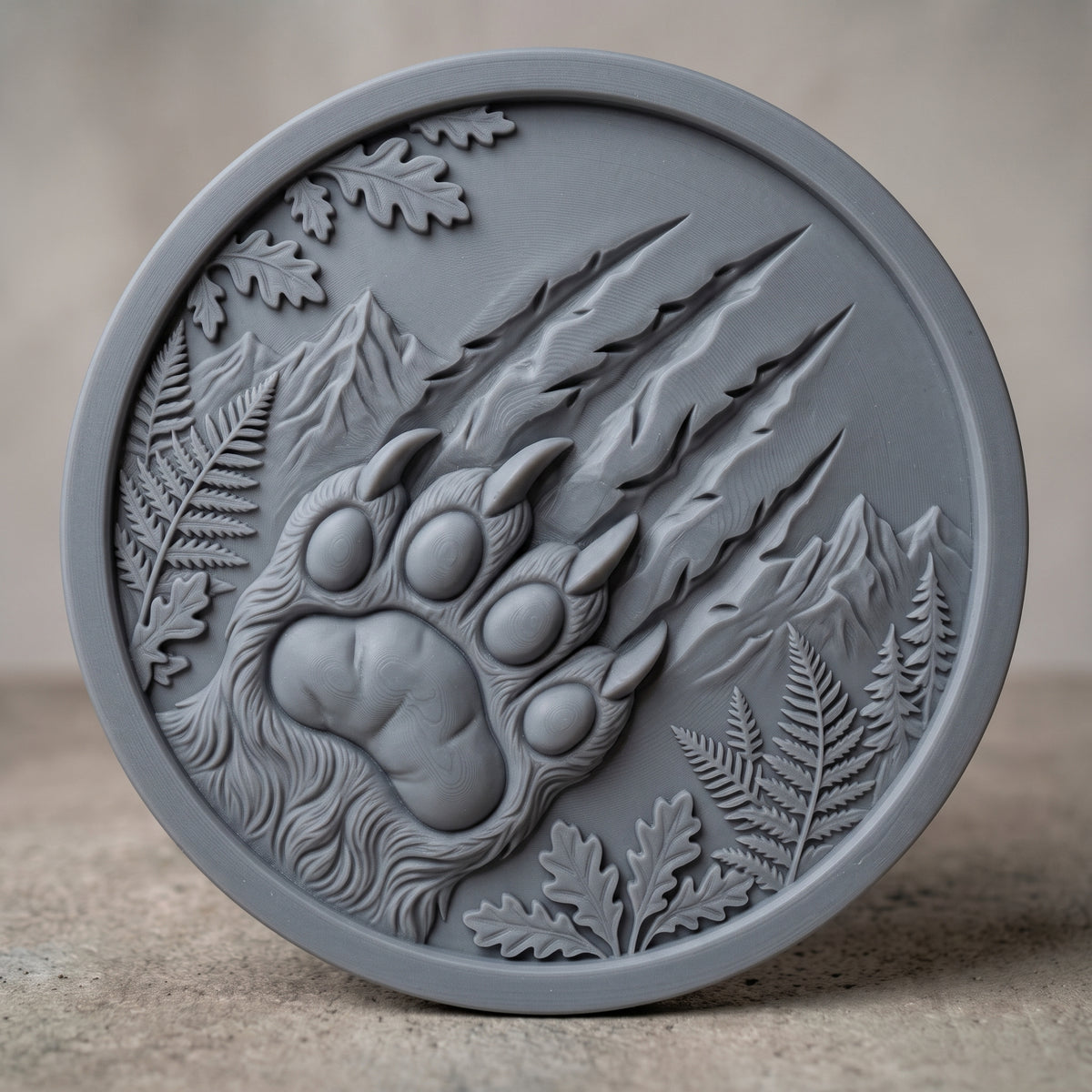 Detailed 3D bas-relief of a large bear paw with four toe pads and curved claws, with deep claw scratch marks slashing across a round medallion. Mountain peaks, ferns, oak leaves and pine trees fill the scene inside a raised ring border. Shown in carved walnut wood and grey resin. Designed for CNC relief carving, woodworking and 3D printing as rustic cabin wildlife wall decor.