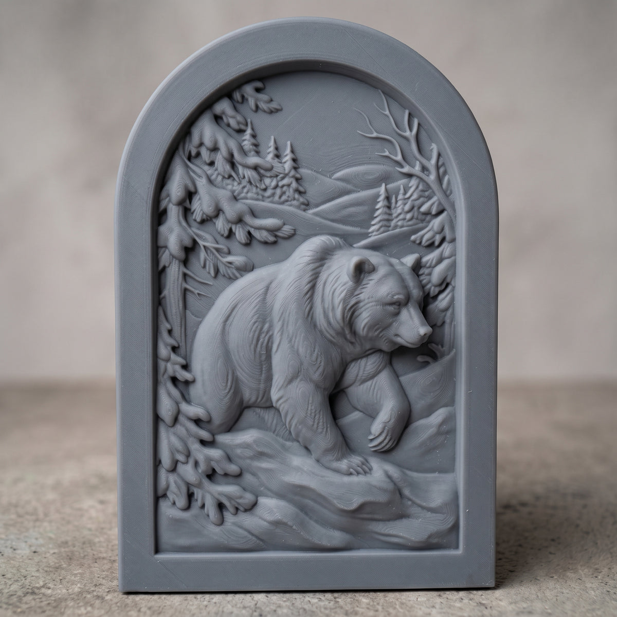Detailed 3D bas-relief of a brown bear walking through a snowy winter forest, front paw raised, with snow-laden pine branches, bare winter branches, distant fir trees and rolling hills. Set in a recessed arched panel with a stepped molded frame. Fine fur and snow texture. Designed for CNC relief carving, woodworking and 3D printing as rustic cabin wall decor.